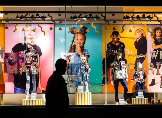 A man walks past a colourful, illuminated shop window in Dundee, Scotland.
