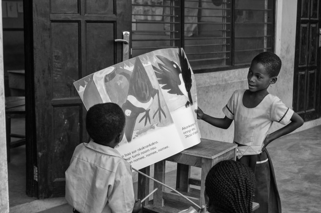 Children in a Ghanaian preschool read a story book with their teacher.